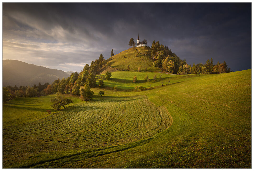Hornatá krajina Slovinska s&nbsp;magickým kostelíkem na&nbsp;samém vrchu jednoho z&nbsp;kopců při západu slunce -Fotografický workshop Pohádkové podzimní Slovinsko.